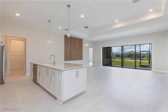 kitchen with sink, white cabinetry, a tray ceiling, decorative light fixtures, and an island with sink