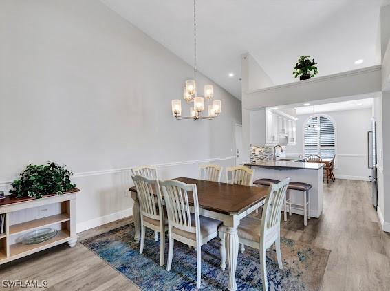 dining room with wood-type flooring, high vaulted ceiling, sink, and a chandelier