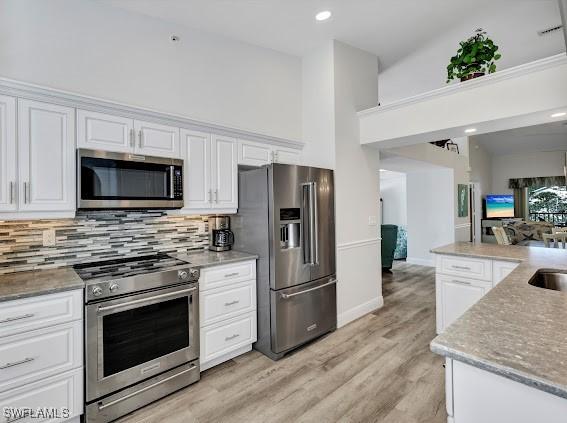 kitchen with appliances with stainless steel finishes, a towering ceiling, white cabinetry, backsplash, and light hardwood / wood-style floors