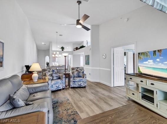 living room featuring high vaulted ceiling, ceiling fan with notable chandelier, and light wood-type flooring