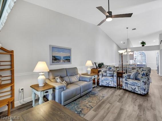 living room with hardwood / wood-style flooring, vaulted ceiling, and ceiling fan with notable chandelier