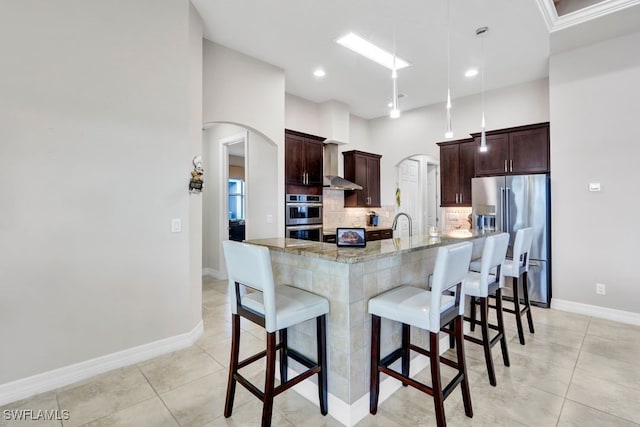 kitchen with light stone counters, decorative light fixtures, a center island with sink, appliances with stainless steel finishes, and decorative backsplash