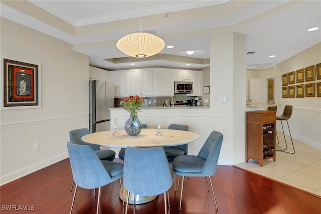 dining area featuring hardwood / wood-style flooring, crown molding, and a raised ceiling