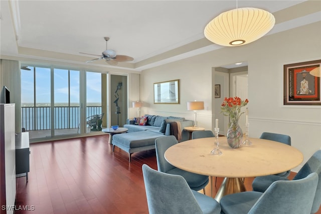 dining space with a water view, ornamental molding, dark hardwood / wood-style flooring, a raised ceiling, and ceiling fan