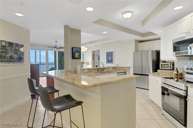 kitchen featuring stainless steel appliances, light stone counters, white cabinets, and a kitchen bar