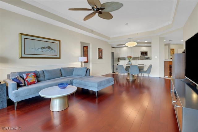 living room with dark hardwood / wood-style flooring, a tray ceiling, crown molding, and ceiling fan