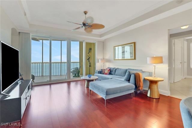 living room featuring hardwood / wood-style flooring, ceiling fan, ornamental molding, and a raised ceiling