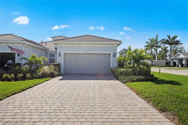 ranch-style home featuring decorative driveway, a tile roof, stucco siding, a front yard, and a garage