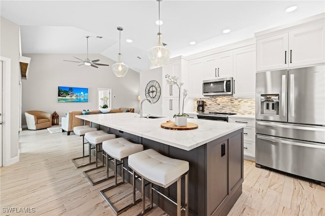 kitchen with sink, a kitchen island with sink, stainless steel appliances, light stone countertops, and white cabinets