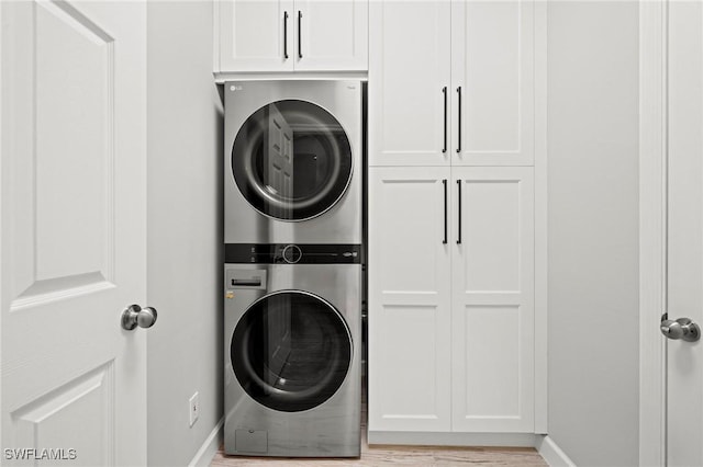 clothes washing area with cabinets, stacked washer / drying machine, and light wood-type flooring