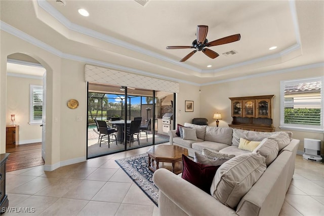 living room featuring crown molding, ceiling fan, a tray ceiling, and light tile patterned floors