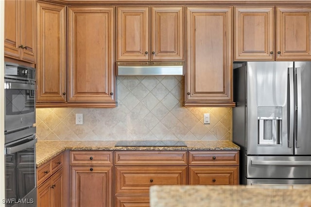 kitchen featuring double oven, light stone countertops, stainless steel fridge with ice dispenser, and tasteful backsplash