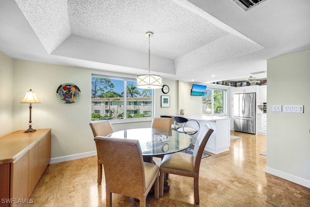 dining space with a tray ceiling, a textured ceiling, and light wood-type flooring