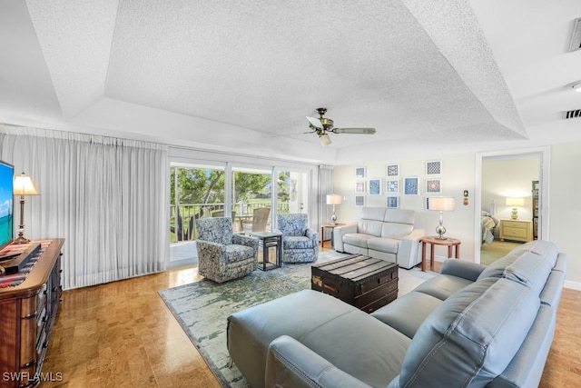 living room with ceiling fan, light hardwood / wood-style flooring, a raised ceiling, and a textured ceiling