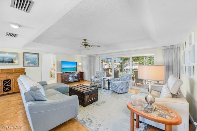 living room with ceiling fan, a raised ceiling, and a textured ceiling