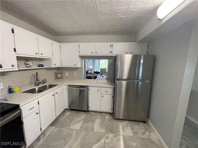 kitchen with a sink, appliances with stainless steel finishes, white cabinets, light countertops, and decorative backsplash