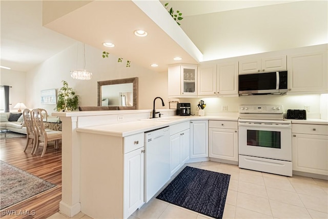 kitchen featuring white appliances, a peninsula, a sink, glass insert cabinets, and open floor plan