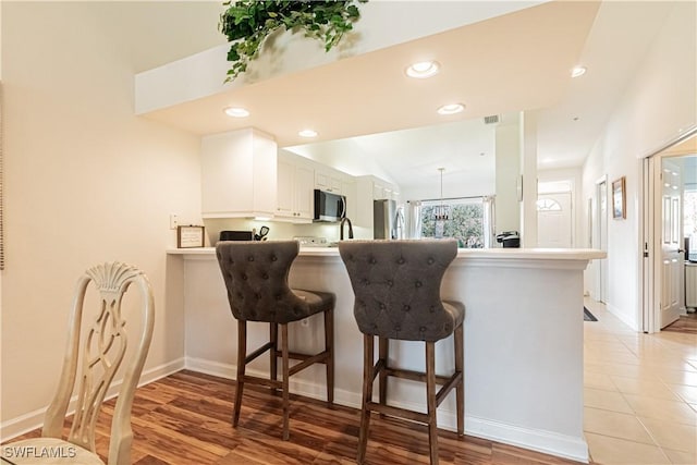 kitchen with a peninsula, recessed lighting, stainless steel appliances, white cabinets, and a kitchen breakfast bar