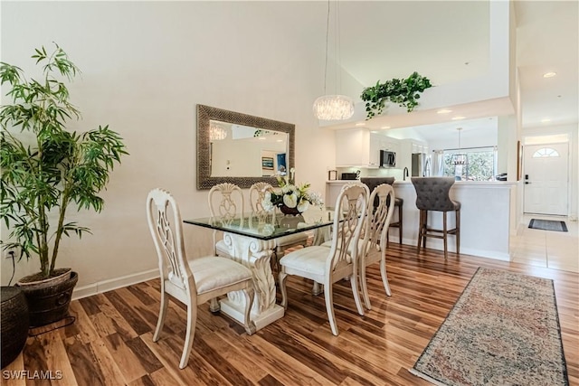 dining area with recessed lighting, baseboards, wood finished floors, and a towering ceiling