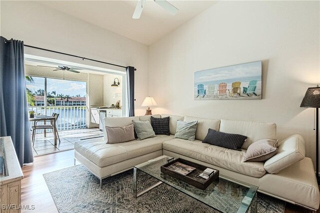 living area with light wood-style floors, a ceiling fan, and vaulted ceiling