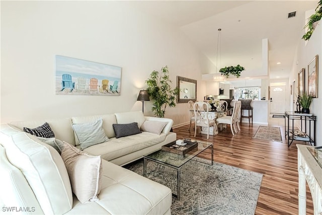 living room with baseboards, wood finished floors, visible vents, and high vaulted ceiling