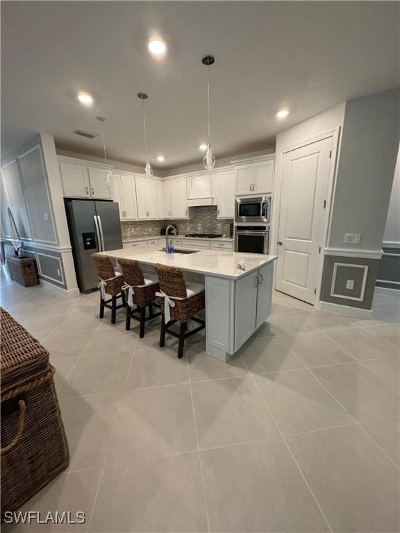 kitchen with white cabinetry, tasteful backsplash, hanging light fixtures, stainless steel appliances, and a kitchen island with sink