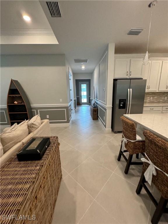 kitchen featuring stainless steel refrigerator with ice dispenser, crown molding, light tile patterned floors, white cabinets, and backsplash