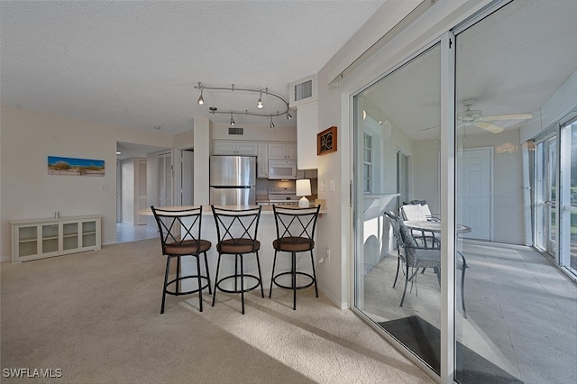 kitchen featuring white cabinetry, stainless steel fridge, light carpet, and a kitchen bar