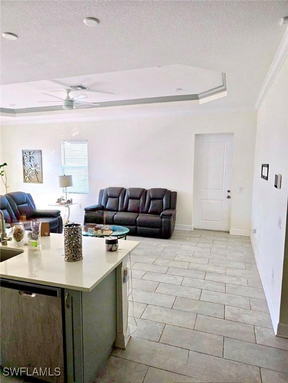 living room with sink, a textured ceiling, ornamental molding, a tray ceiling, and ceiling fan