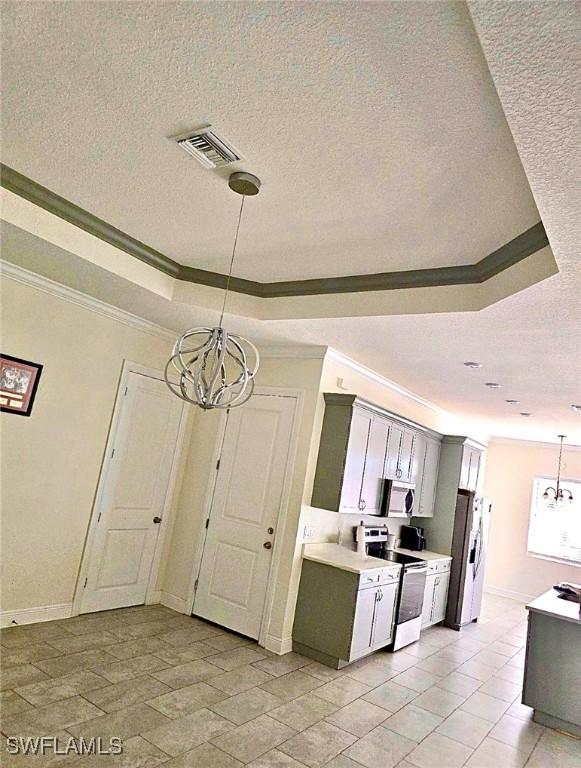 kitchen with appliances with stainless steel finishes, pendant lighting, a chandelier, ornamental molding, and a raised ceiling