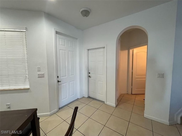 interior space with arched walkways, light tile patterned floors, and baseboards