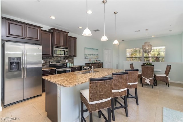 kitchen with sink, light stone counters, pendant lighting, stainless steel appliances, and a kitchen island with sink