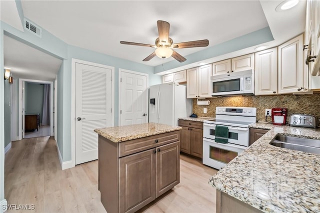 kitchen featuring light stone countertops, a center island, white appliances, and decorative backsplash