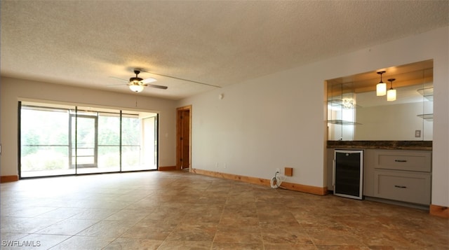 unfurnished living room featuring a dry bar, beverage cooler, baseboards, a ceiling fan, and a textured ceiling