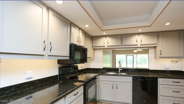 kitchen with dark stone countertops, a tray ceiling, black appliances, a sink, and recessed lighting