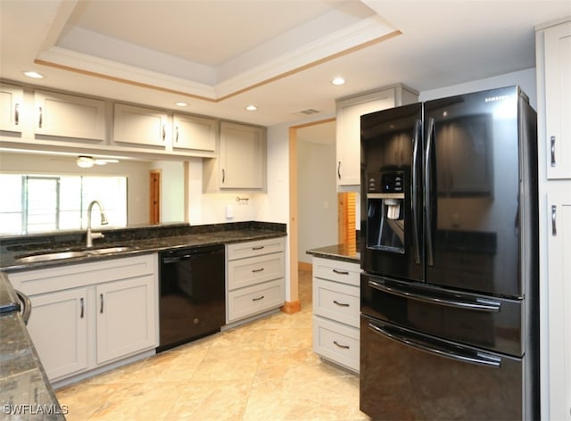 kitchen with dark stone counters, black appliances, a tray ceiling, and a sink