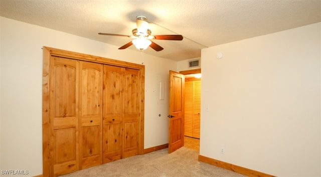 unfurnished bedroom with a textured ceiling, light colored carpet, visible vents, baseboards, and a closet