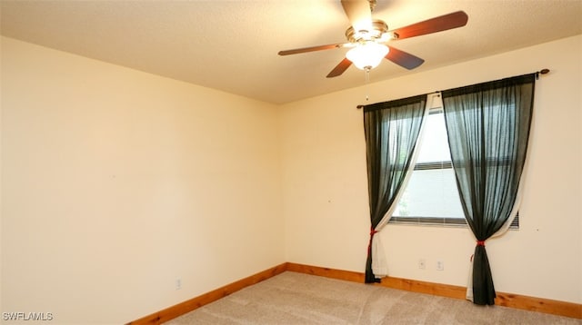 empty room with a textured ceiling, ceiling fan, baseboards, and light colored carpet