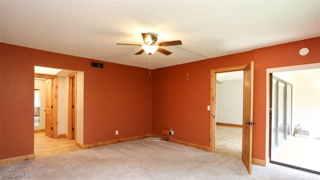 spare room with light colored carpet, visible vents, a ceiling fan, a textured ceiling, and baseboards