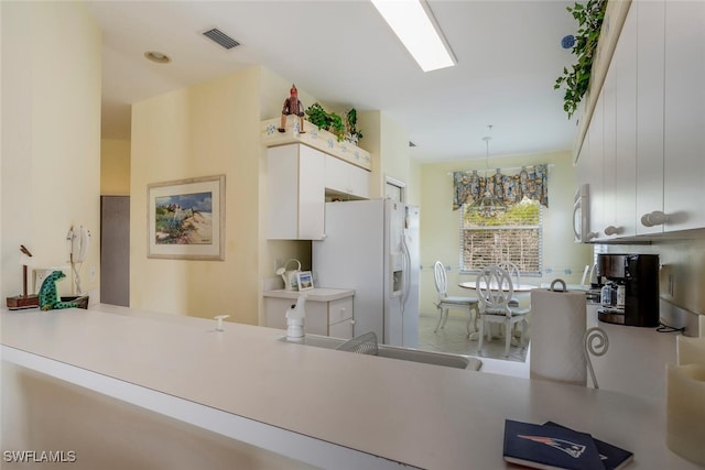 kitchen with decorative light fixtures, white appliances, kitchen peninsula, and white cabinets