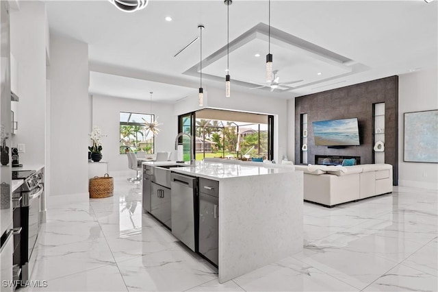 kitchen with stainless steel appliances, hanging light fixtures, a center island with sink, and a tray ceiling