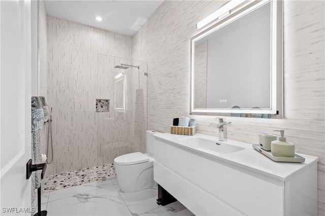 bathroom featuring vanity, toilet, tile walls, and a tile shower