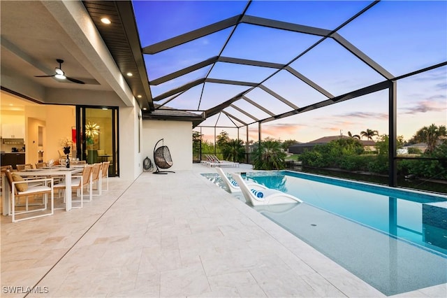 pool at dusk featuring a patio, ceiling fan, and glass enclosure