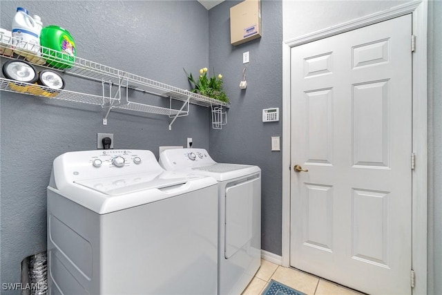 clothes washing area featuring laundry area, a textured wall, light tile patterned flooring, and independent washer and dryer