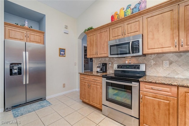 kitchen with light stone countertops, arched walkways, stainless steel appliances, and decorative backsplash