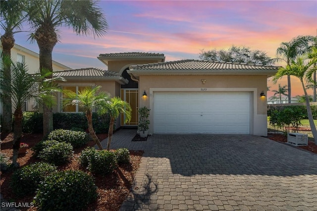 mediterranean / spanish-style house featuring a garage, a tiled roof, decorative driveway, and stucco siding