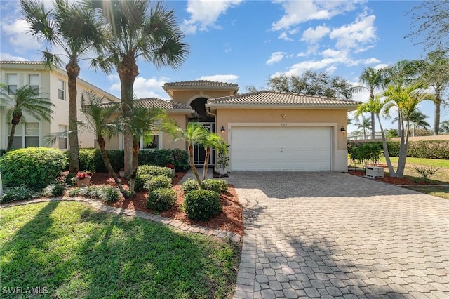 mediterranean / spanish house with a garage, a tile roof, decorative driveway, a front lawn, and stucco siding