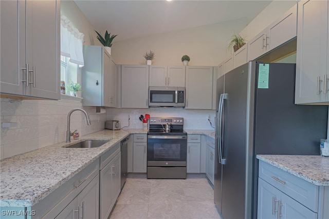 kitchen with sink, light stone counters, appliances with stainless steel finishes, gray cabinets, and backsplash