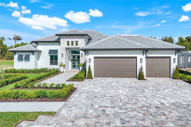 prairie-style house with stucco siding, an attached garage, and decorative driveway