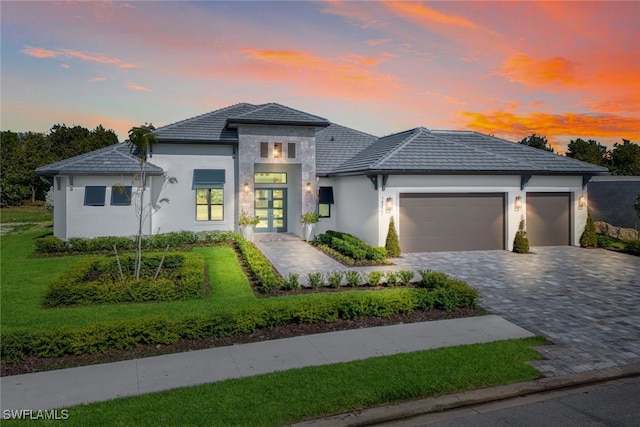 view of front of home with stucco siding, decorative driveway, a yard, and a garage